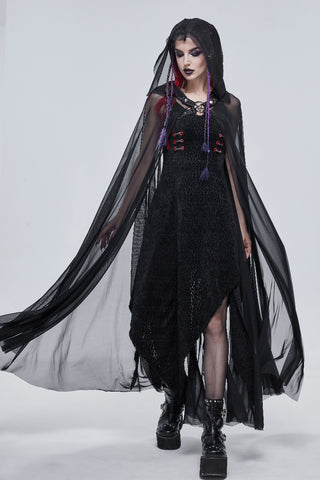 Full-body view of a woman in a sheer black hooded cape walking forward, with dark makeup and platform boots, against a white backdrop.