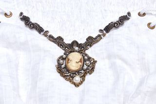 Close-up of antique bronze cameo pendant detail on white gothic dress neckline