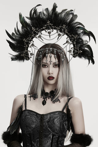 Woman in a black lace corset and dramatic black feather headdress with chains and jewels, posed against a white background.
