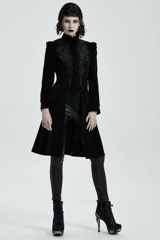 Model in punk rave wy-1306 a long black Gothic velvet coat with ornate embroidery, corset back, and structured shoulders, paired with black leggings and platform heels on a white background