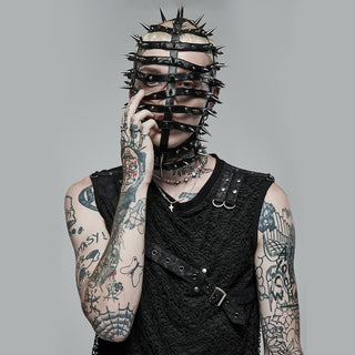 Tattooed model wearing a black textured sleeveless top and full-face spiked leather mask, styled for a dark carnival or freakshow fashion look.