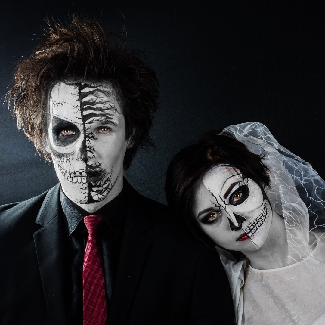 Gothic bride and groom in skeleton makeup and dark formalwear, leaning together in dramatic wedding portrait