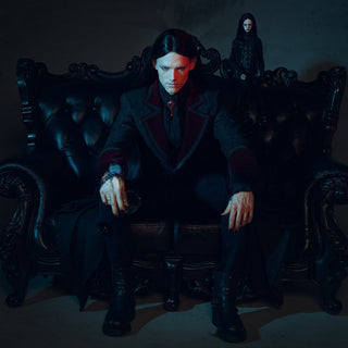 Man in Gothic coat sitting on dark baroque sofa with intense expression