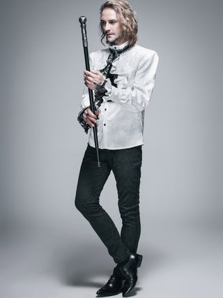 Man in a white shirt with ruffled details and black pants holding a cane on a gray background
