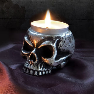 Antique silver skull tea light holder with a lit candle on a dark fabric background
