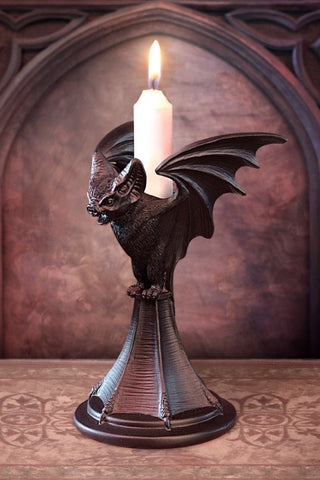Black bat taper candle holder with a lit white candle displayed in a gothic room