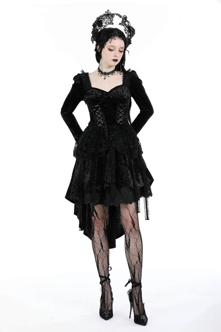 Model wearing a black Gothic high-low dress with corset bodice and lace sleeves, hands on hips, white background.