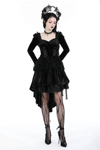 Woman wearing a black Gothic lace dress with corset bodice, high-low skirt, patterned tights, and ornate lace crown – standing with arms on hips against a white background.