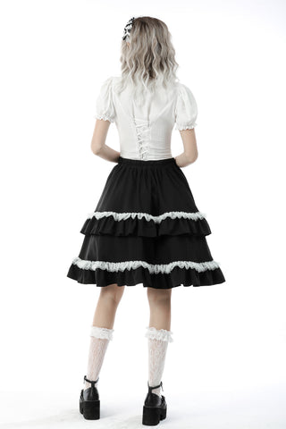 Back view of model wearing a white puff-sleeve blouse with corset-style lacing and a tiered black skirt with white lace trim – on white background.