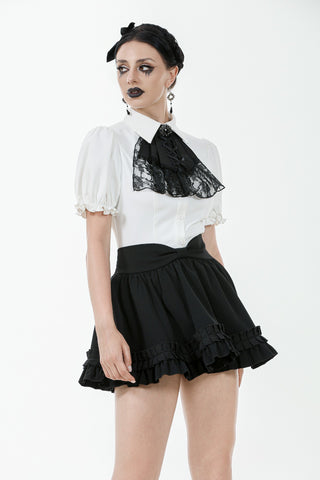 Model wearing a white puff-sleeve blouse with black lace cravat and high-waisted black ruffle skirt, standing against a white background