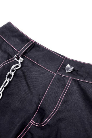 Close-up of black waistband with pink contrast stitching, silver heart button, and attached metal chain detail