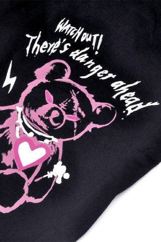 Close-up of pink graffiti teddy bear print with white text reading “Watch out! There’s danger ahead” on black fabric