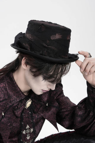 Person wearing a distressed black Victorian-style top hat with layered fabric details, paired with a burgundy gothic shirt featuring cross and cameo brooches, looking downward against a white background.