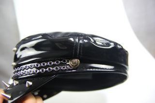 Close-up of black patent cap with chain detail and metal studs