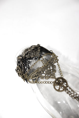 Angled close-up of Devil Fashion AS057 Steampunk bracelet ring chain displayed on a clear mannequin hand, showing brass gears, filigree design, and lace cuff detail.