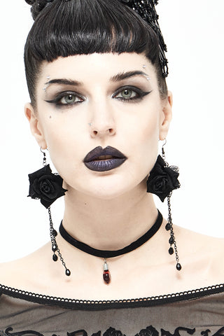 Woman wearing long black rose drop earrings with cascading bead chains and a black choker, against a white background.