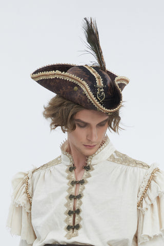 A man modeling a pirate costume consisting of a cream ruffled shirt with gold trim, and a black tricorn hat with a feather, set against a plain white studio background.