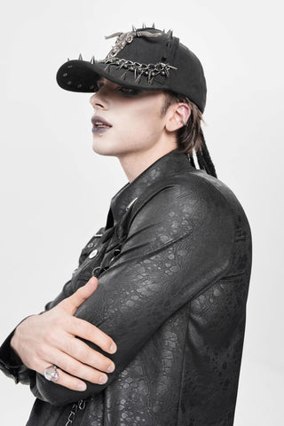 Side view of black spiked cap with horned skull emblem and chain trim, worn with a black textured jacket and crossed arms.