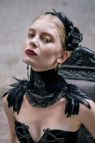 Model wearing a black gothic high collar with embroidered front detail, net frills and feathers across the shoulders.