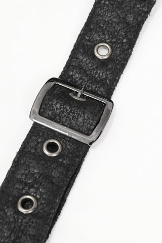 Close-up of a black cracked faux leather strap with a square silver buckle and metal grommets, laid diagonally on a white surface.