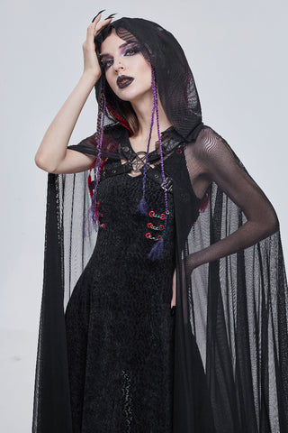 Close-up of a woman posing in a sheer black hooded cape over a textured black dress, with her hand raised to her head.