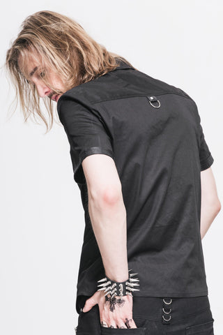 Man showing back view of a black short-sleeve shirt with faux leather panels and a metal D-ring detail, against a white background.
