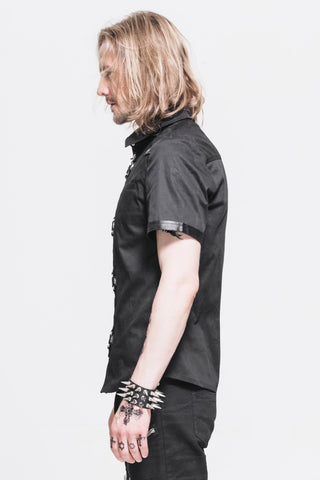 Man in profile view wearing a black short-sleeve shirt with faux leather trim and metal ring details, against a white background.