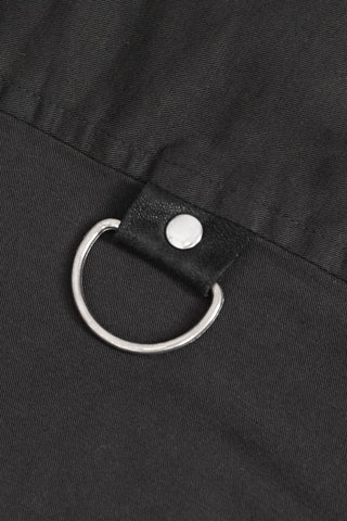 Close-up of a silver D-ring attached with a black faux leather strap and snap button on dark fabric.