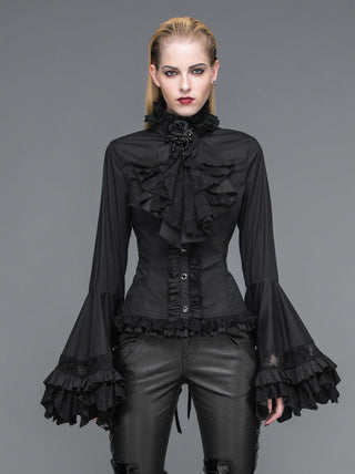 Model wearing a black Victorian‑style ruffled blouse with flared lace sleeves and a high neck, paired with black pants, against a grey background.