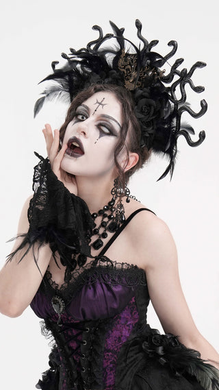 Model in Gothic Medusa headband with sculpted snakes, black feathers, and Victorian corset dress, posing with theatrical expression on white background.