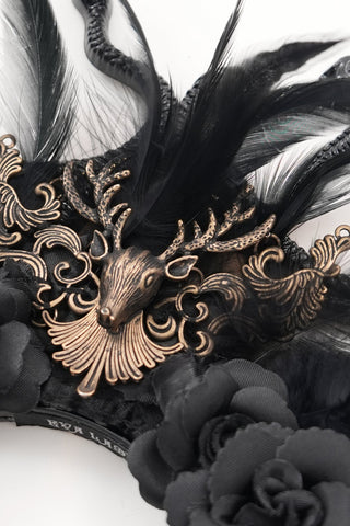 Close-up of antique gold deer crest with ornate detailing, black feathers, and black fabric roses on Gothic headpiece.