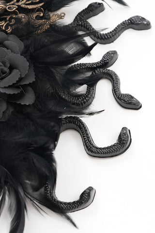 Close-up of black sculpted snakes and fabric flowers on a Gothic headpiece with black feathers, on a white background