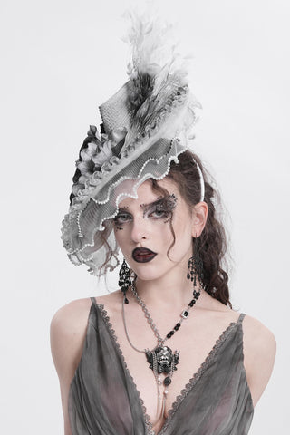 Gothic woman wearing a grey Victorian hat with lace, roses, and feathers, styled with dark makeup and layered jewellery against a white background.