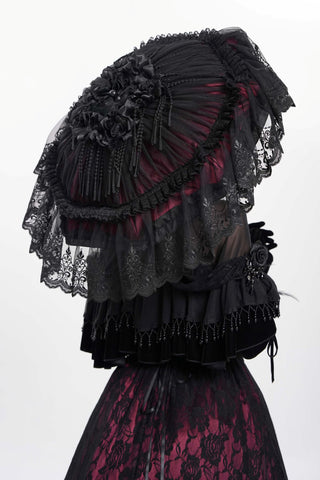 Close-up back view of a black lace Victorian-style parasol with layered ruffles, rosette accents, and embroidery, held over a black and red lace gown against a white background.