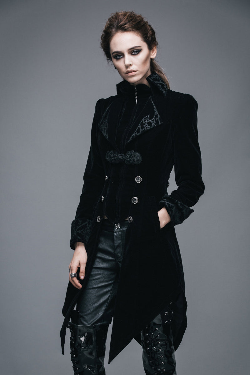 Woman wearing a dramatic Gothic black velvet tailcoat with ornate buttons, brocade lapels, and asymmetrical hem, styled with black leather pants