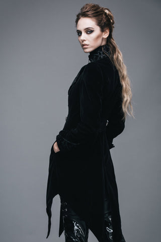 Side view of a woman wearing a Gothic black velvet tailcoat with brocade collar and pointed hem, hands in pocket