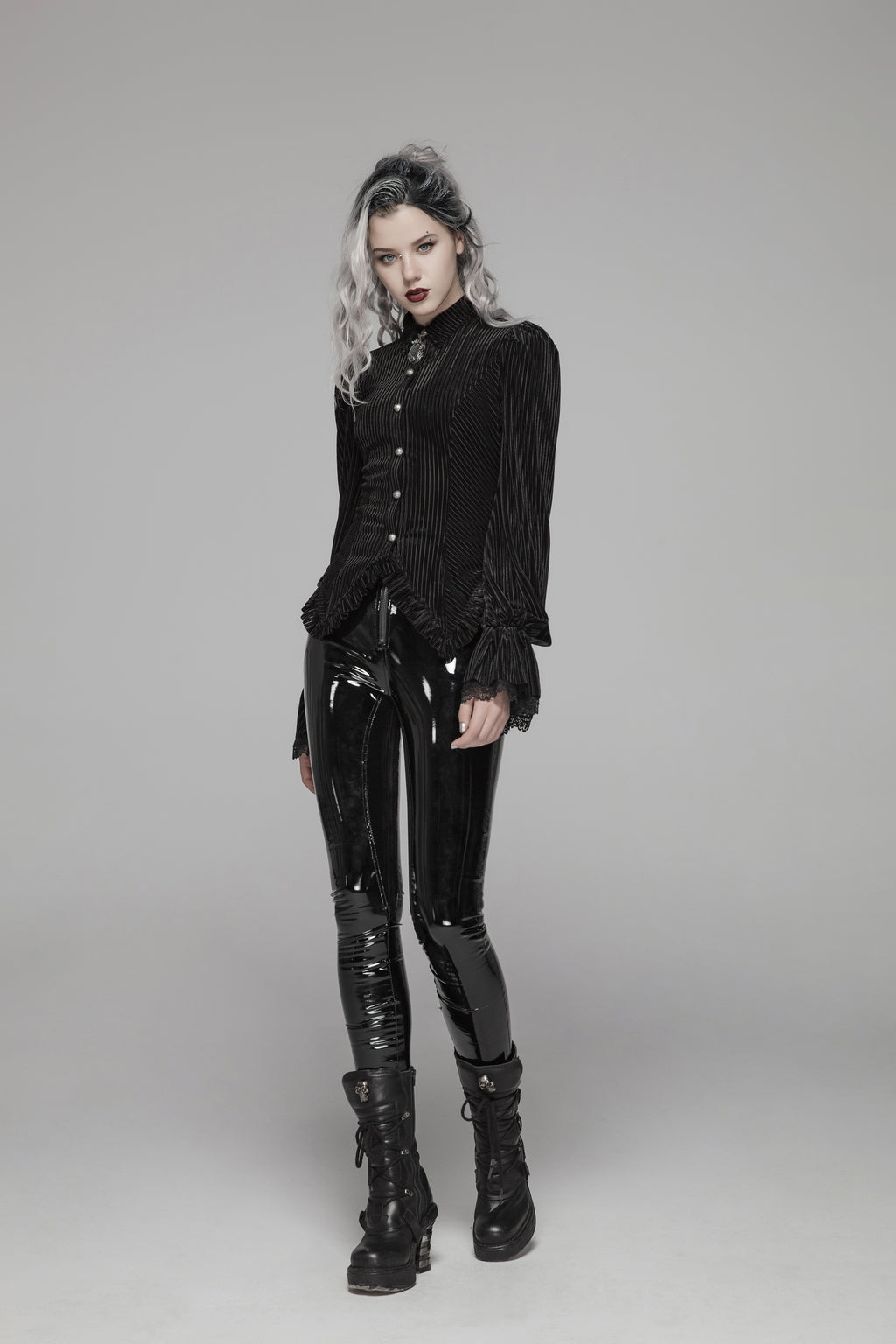 Model in a black striped button-front blouse with puff shoulders, fluted lace cuffs, and a pointed hem, turning to show the corset-laced back on a gray background.