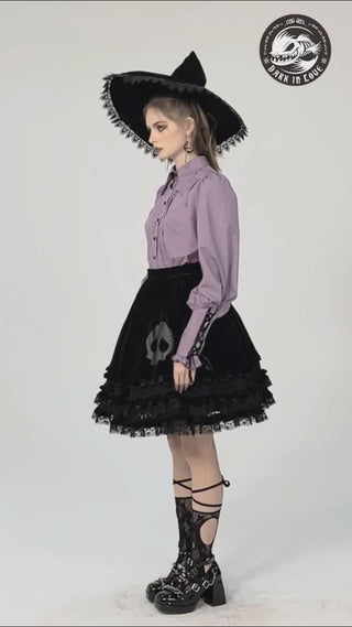 Model in light violet witchy blouse with puff sleeves and bat-shaped collar, paired with black lace skirt featuring skull detail, wide-brim hat, and platform heels.