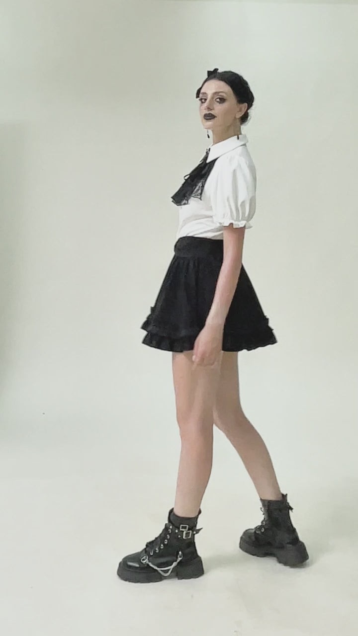 Model wearing white puff-sleeve blouse with black lace cravat, standing and shifting subtly against a white background
