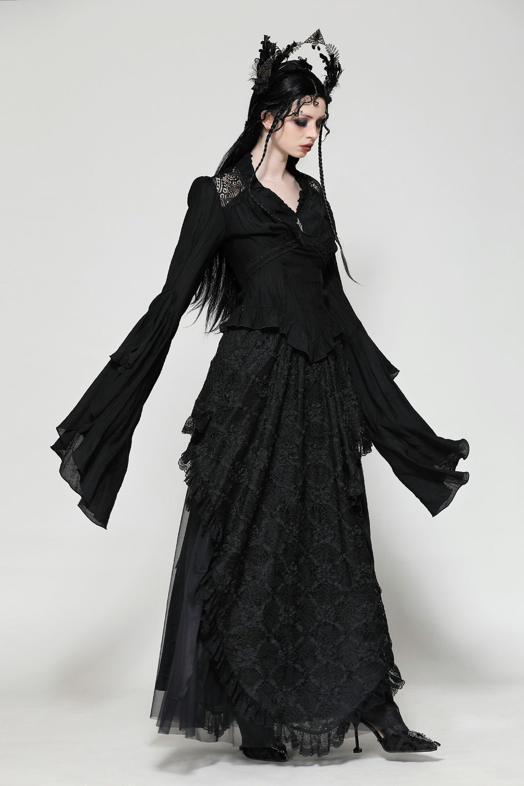 Woman wearing dark in love tw-624 a black Gothic Victorian top with flared bell sleeves, lace accents, and layered hem, styled with a matching long skirt and headpiece