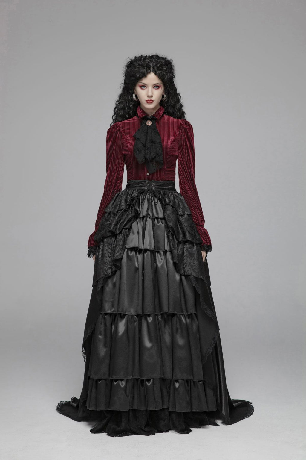 Model in a red striped button-front blouse with puff shoulders, fluted lace cuffs, and a pointed hem, turning to show the corset-laced back on a gray background.