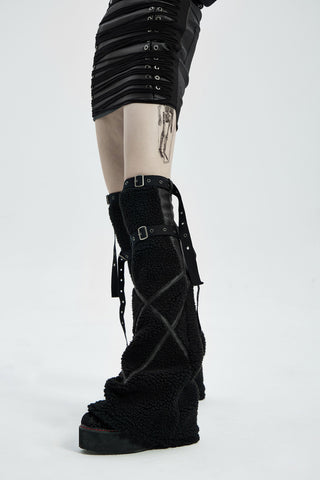 Close-up of black flared sherpa legwarmers with buckle straps worn over platform boots, shown from the side.