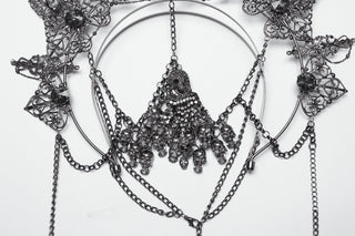 Close-up of an ornate silver Gothic crown with intricate filigree, gemstone accents, and dangling skull charms, displayed on a white background.