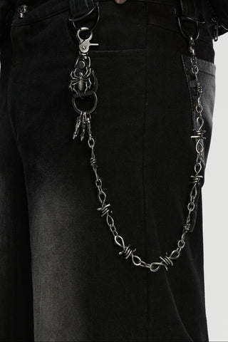 Close-up of a barbed-wire style chain keychain with a spider clip, attached to black pants.