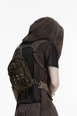 Side angle view of model wearing brown distressed cyber goth utility sling bag with skull chain detail