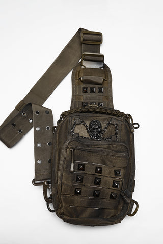 Brown distressed utility sling bag with skull hardware, studded front pocket and adjustable crossbody strap on white background