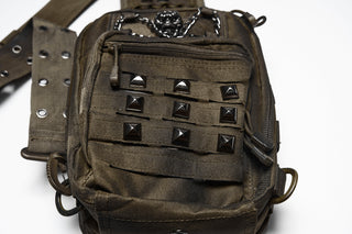 Close-up of studded front pocket and utility strap details on brown distressed sling bag