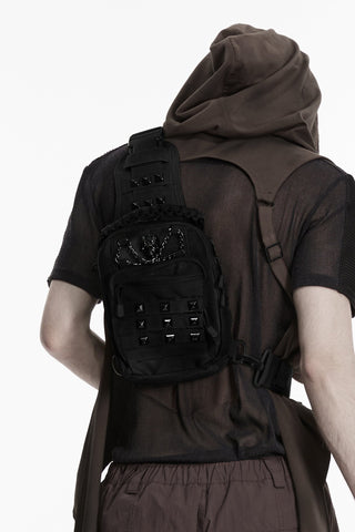 Back view of model wearing black utility sling bag with skull hardware and adjustable crossbody strap