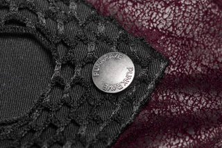 Macro shot of a metal button embossed with “PUNK RAVE” on a black textured mesh panel, layered over deep burgundy patterned fabric.