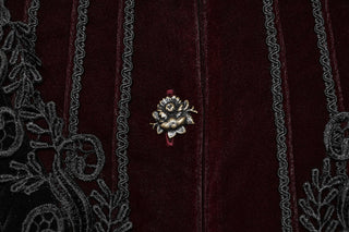 Close-up of antique gold rose button on burgundy velvet panel with black embroidered trim